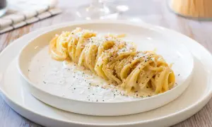 Un plat de tonnarelli cacio e pepe, des pâtes crémeuses saupoudrées de fromage et de poivre noir, sur une assiette blanche.
