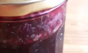 Un pot de confiture de raisin noir, avec des morceaux de fruits visibles, prêt à être dégusté.
