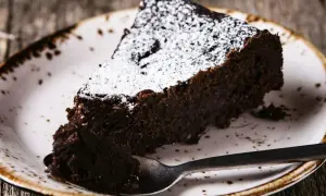 Une part de torta tenerina, un gâteau au chocolat intense, saupoudrée de sucre glace, sur une assiette rustique.