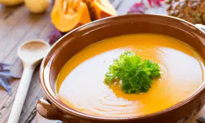 Soupe potimarron onctueuse, garnie de persil frais, dans un bol en terre cuite. Des morceaux de potimarron et une cuillère en bois complètent cette scène automnale.