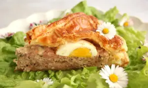 Tranche de pâté de Pâques savoureux, garni d'un œuf dur, sur un lit de salade verte et décoré de pâquerettes.
