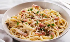 Un plat de carbonara romaine crémeuse, garni de lardons, de persil frais et de parmesan râpé. Un délice !