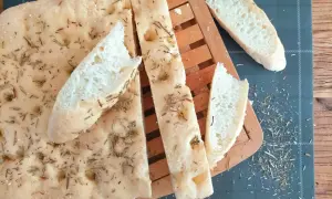 Délicieuse focaccia sans gluten, parsemée de romarin et de sel, coupée en tranches sur une planche en bois.
