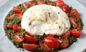 Une délicieuse recette burrata froide avec des tomates cerises coupées, du pesto et une touche de poivre noir.