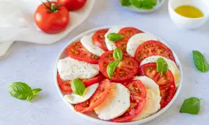 Salade Caprese al limone : rondelles de tomates fraîches, mozzarella crémeuse et feuilles de basilic, assaisonnée d'un filet d'huile d'olive.