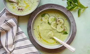 Deux bols de soupe froide crémeuse aux concombres, garnie de rondelles de concombre, de menthe et d'un filet d'huile d'olive.