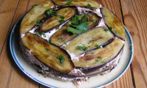 Moussaka ronde, une délicieuse moussaka ricetta, garnie d'aubergines grillées et de persil frais, sur une assiette blanche à bordure verte.