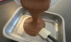 Une spatule aide à verser une ganache chocolat onctueuse dans un plat métallique.