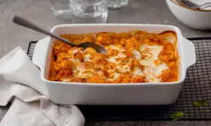Un plat blanc rempli de gnocchi alla sorrentina, gratinés au fromage fondant et à la sauce tomate. Une cuillère est prête à servir.