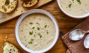 Deux bols de velouté de champignons à la crème, garni de persil et de poivre, avec des tranches de pain croustillant sur une planche en bois.