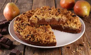 Une délicieuse tarte aux poires, avec une croûte croustillante et des morceaux de chocolat noir, est présentée sur une assiette blanche.