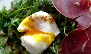 Salade lyonnaise avec œuf poché coulant, roquette et fines tranches de viande séchée.