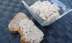 Deux tranches de pain de campagne garnies de rillettes de thon, avec un bol de rillettes de thon en arrière-plan.