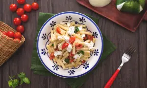 Un plat de pâtes alla checca, garni de tomates cerises fraîches, de mozzarella et de basilic, prêt à être dégusté.