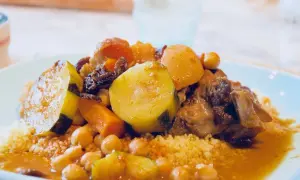 Un plat généreux de couscous algérien, garni de légumes tendres, de pois chiches et de viande savoureuse, baignant dans une sauce parfumée.