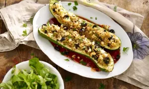 Deux courgettes farcies végétariennes, garnies de riz, olives et feta, sur un lit de sauce tomate. Une salade verte accompagne ce plat.