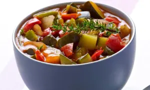 Un bol de ratatouille niçoise, un plat coloré de légumes mijotés, garni d'une branche de thym frais.