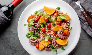 Salade de poulpe fraîchement préparée, garnie d'oranges, de tomates cerises et de verdure, prête à être dégustée avec une bouteille de vin rouge.