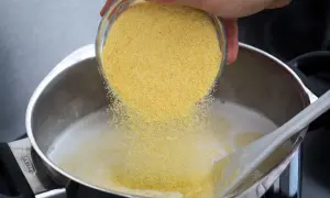 Une main verse de la semoule dans une casserole de lait chaud pour préparer un délicieux semoule au lait.