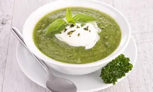 Soupe froide courgette fromage frais, garnie de basilic et persil. Une cuillère repose à côté du bol.