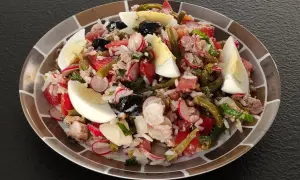 Salade niçoise revisitée avec du riz, garnie d'œufs durs, de thon, de haricots verts, de tomates, de radis et d'olives noires.