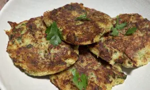 Galettes dorées de courgette et pomme de terre, garnies de persil frais, présentées dans un plat blanc.