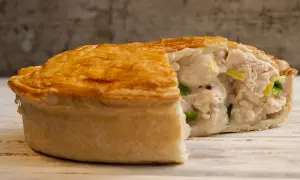 Une tourte au poulet dorée et croustillante, coupée pour révéler une garniture crémeuse et généreuse de poulet et de légumes verts.
