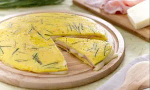 Une délicieuse omelette farcie aux herbes, jambon et fromage fondant, coupée en part pour un repas savoureux.
