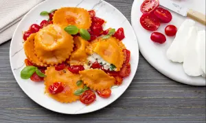 Ravioli caprese orange vif, farcis de ricotta et basilic, servis avec des tomates cerises et une sauce légère.