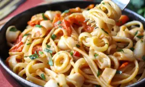 Une assiette de pâtes aux calamars italienne, garnie de persil frais et de morceaux de tomates. Une fourchette soulève une portion de ce plat savoureux.
