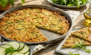 Une délicieuse scarpaccia de courgettes, dorée et garnie de fromage râpé, est servie sur une table en bois ensoleillée.