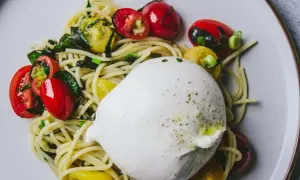 Délicieuse recette avec burrata : pâtes, tomates cerises rouges et jaunes, et herbes fraîches sur une assiette.