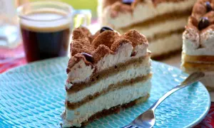 Une part de tiramisu gâteau, crémeux et aérien, saupoudrée de cacao, avec un café noir en arrière-plan.