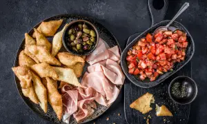Assiette de gnocco fritto croustillant, olives, mortadelle et prosciutto, avec une salade de tomates fraîches.