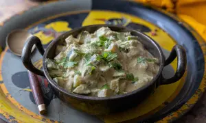 Un plat de courgettes au curry crémeux, garni de coriandre fraîche, servi dans un bol en métal sur un plateau décoré.