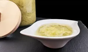 Une coupelle blanche présente une compote de rhubarbe onctueuse, avec un bocal en verre rempli de cette même compote en arrière-plan.