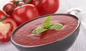 Un bol de soupe de tomates fraîches, garni de basilic, avec des tomates mûres en arrière-plan.