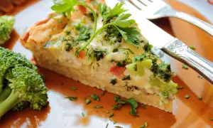 Une part de tarte aux légumes, garnie de persil frais, est servie sur une assiette orange avec du brocoli.