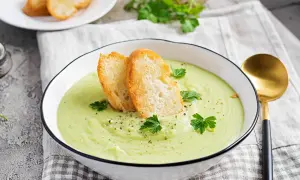 Un bol de soupe verte onctueuse, garnie de croûtons dorés et de persil frais. Parfait pour une recette gaspacho méditerranéen.