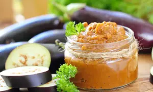 Un pot de caviar d'aubergine, prêt à être dégusté, avec des aubergines fraîches et des herbes. Une recette italienne simple et savoureuse.