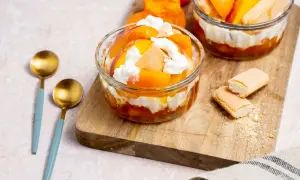 Deux coupes de dessert healthy aux pêches et crème fouettée, garnies de biscuits à la cuillère.