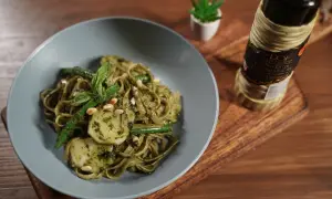 Assiette de trenette al pesto, garnie de haricots verts, pignons de pin et basilic frais. Une bouteille d'huile d'olive est visible à côté.