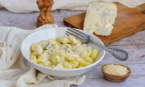 Gnocchi al gorgonzola crémeux dans un bol blanc, avec un morceau de gorgonzola sur une planche à découper en arrière-plan.