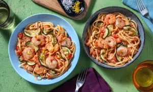 Deux assiettes de linguine crevettes courgettes, garnies de zeste de citron. Un plat savoureux et coloré.