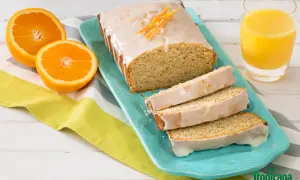 Un délicieux pain d'orange glacé, garni de zestes d'orange, servi avec des moitiés d'orange et un verre de jus d'orange.