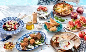 Idée apéro rapide sans cuisson : salade grecque, houmous, pain pita, feuilletés, bruschettas et olives, le tout près d'une piscine.