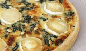 Quiche épinard chèvre, garnie de rondelles de fromage de chèvre et de pignons de pin, prête à être dégustée.