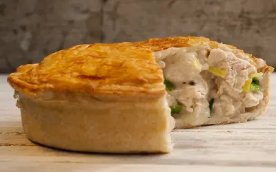 Une tourte au poulet dorée et croustillante, coupée pour révéler une garniture crémeuse et généreuse de poulet et de légumes verts.
