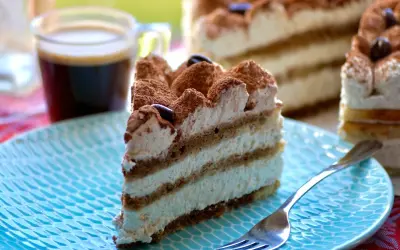 Une part de tiramisu gâteau, crémeux et aérien, saupoudrée de cacao, avec un café noir en arrière-plan.