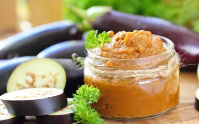 Un pot de caviar d'aubergine, prêt à être dégusté, avec des aubergines fraîches et des herbes. Une recette italienne simple et savoureuse.